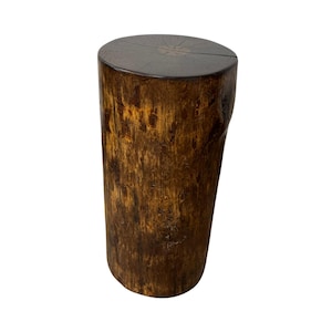 Puede incluir: Un taburete o mesa auxiliar cil&iacute;ndrica de madera que presenta un exterior de corteza texturizada de color marr&oacute;n oscuro y una superficie superior lisa y plana que muestra patrones de veta de madera y un detalle de anillo central.