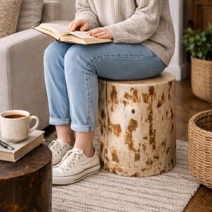 Puede incluir: Un taburete cil&iacute;ndrico de madera con una veta natural de color claro, manchas marrones prominentes y un acabado liso y pulido. El taburete funciona como un asiento bajo y resistente con una superficie superior plana y una estructura s&oacute;lida.
