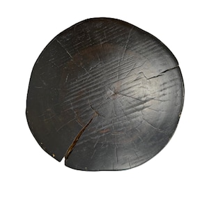 Puede incluir: Un asiento de taburete circular de madera con un acabado te&ntilde;ido en marr&oacute;n oscuro. La superficie muestra un patr&oacute;n de veta de madera natural prominente, anillos de crecimiento visibles y varias grietas estructurales profundas desde el centro.