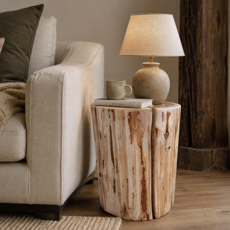 Pu&ograve; includere: Un tavolino cilindrico ricavato da un tronco d'albero naturale di colore chiaro con una fessura verticale. Sopra poggia una lampada da tavolo in ceramica beige con paralume conico in tessuto, una piccola tazza in ceramica abbinata e un libro.