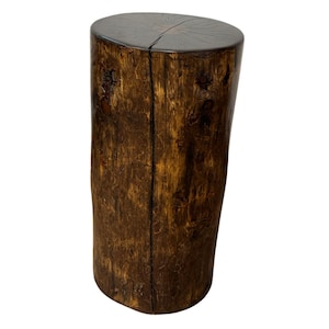 Puede incluir: Un taburete o mesa auxiliar cil&iacute;ndrica de madera con un acabado pulido en color marr&oacute;n oscuro. La superficie muestra vetas naturales de madera y una grieta vertical prominente en el lateral, con una parte superior lisa y plana con l&iacute;neas radiales.