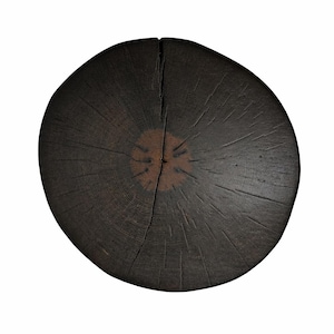 Puede incluir: Una rodaja de madera circular con un acabado marr&oacute;n oscuro carbonizado. La superficie muestra un anillo central prominente en un tono marr&oacute;n m&aacute;s claro, rodeado de profundas vetas radiantes y una grieta vertical que va del centro al borde.