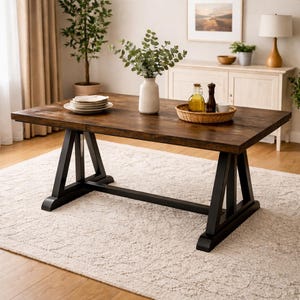 May include: A rectangular wooden dining table with a dark brown finish and black trestle base. The table is set with white plates, a white vase with greenery, and a woven tray with bottles. The table is on a cream-colored rug.