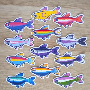 May include: A collection of twelve fish-shaped stickers, each featuring a unique colour combination. The designs include various stripes and gradients in shades of yellow, pink, blue, purple, orange, and green, all with a white border outline.