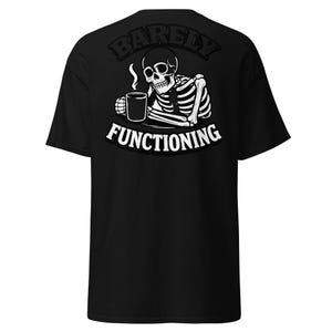 May include: Black t-shirt featuring a white skeleton graphic holding a coffee mug. The text "BARELY" is arched above the skeleton, and "FUNCTIONING" is arched below. The design is centered on the back of the shirt.