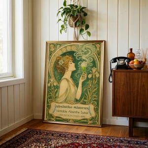 May include: A framed art print featuring an Art Nouveau style illustration of a person holding a glass of green liquid. The text reads Absinthe Mimeux, Veritable Absinthe Suisse, and EXPOSITION PARIS 1889, surrounded by green floral motifs.