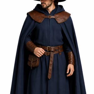 May include: A dark blue hooded cloak featuring brown leather shoulder pauldrons with a buckle closure. The outfit includes a matching brown leather belt with a small attached pouch and brown leather wrist bracers, all secured with metal buckles.