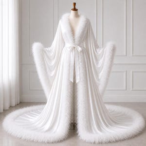 May include: A floor-length white satin robe featuring long, flowing sleeves and a deep V-neckline. The garment is trimmed with white feather detailing along the front opening, the sleeve cuffs, and the hem, and includes a matching satin tie belt.