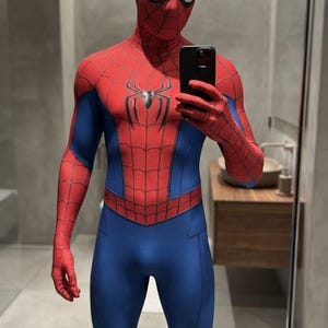 May include: A full-body Spider-Man costume featuring a red and blue spandex-like material with a black web pattern printed across the red sections. The suit includes a mask with large white eye lenses and a black spider emblem centered on the chest.