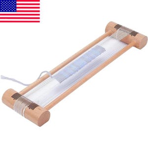 May include: A wooden weaving loom with white threads stretched across. The loom has a light-colored wood frame and cylindrical end pieces. A partially woven blue and white section is visible in the center. The loom is designed for small weaving projects.