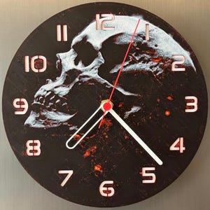 Könnte beinhalten: Eine runde, schwarze Wanduhr mit einem weißen Totenkopfmotiv. Das Zifferblatt hat weiße Ziffern und Zeiger, mit einem roten Sekundenzeiger. Das Totenkopfmotiv ist ein auffälliges Merkmal, das der Uhr ein unverwechselbares, gotisches Aussehen verleiht.