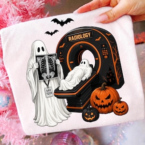 May include: A white t-shirt featuring a graphic of a ghost dressed as a radiologic technologist holding an X-ray of a rib cage, standing next to a CT scanner with a ghost patient inside, two jack-o'-lanterns, and bats with the text RADIOLOGY.