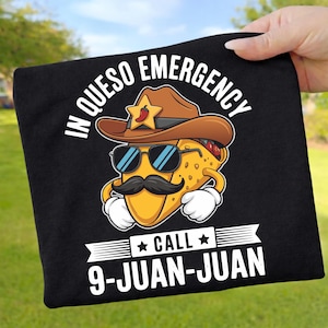 Könnte beinhalten: Schwarzes T-Shirt mit einem Cartoon-Taco, der einen Cowboyhut, eine Sonnenbrille und einen Schnurrbart trägt. Der Text lautet "IN QUESO EMERGENCY CALL 9-JUAN-JUAN". Der Taco hat weiße Handschuhe und einen roten Chili-Pfeffer auf seinem Hut.