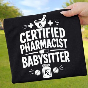 Könnte beinhalten: Ein schwarzes T-Shirt mit weißem Grafiktext, der CERTIFIED PHARMACIST BABYSITTER lautet. Das Design enthält einen Mörser mit Stößel, eine Kapsel, eine Medikamentenflasche mit Rx-Symbol und zwei Pluszeichen, die um den Text angeordnet sind.