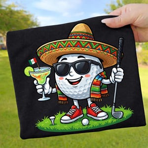 Könnte beinhalten: Schwarzes T-Shirt mit einer Cartoon-Golfballfigur, die eine Sonnenbrille, einen Sombrero und eine farbenfrohe Serape trägt. Der Golfball hält eine Margarita und einen Golfschläger und steht auf einem grünen Golfplatz mit Tee und Ball.
