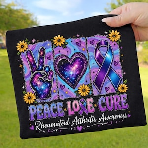 May include: A black t-shirt featuring a graphic with a galaxy-patterned peace sign, a heart, and a blue and purple awareness ribbon. The design includes yellow flowers, stars, and the text PEACE LOVE CURE Rheumatoid Arthritis Awareness.