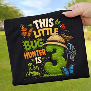 Peut inclure: Un t-shirt noir avec un motif portant le texte THIS LITTLE BUG HUNTER IS 3. Le design comprend un grand chiffre trois vert texturé portant un chapeau de safari beige, un filet à papillons, un papillon monarque, une coccinelle et une mante.