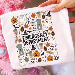 Könnte beinhalten: Ein weißes T-Shirt mit einem Grafikdruck mit dem Text EMERGENCY DEPARTMENT, umgeben von Halloween- und medizinischen Symbolen wie Kürbissen, Geistern mit Krankenschwesterhauben, Stethoskopen, Arztkitteln, Spritzen, Totenköpfen und Herbstblättern.