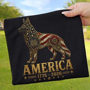 May include: A black t-shirt featuring a graphic of a German Shepherd dog filled with a gold, red, and blue American flag pattern, stars, and fireworks. Below the dog, the text reads AMERICA 1776 - 2026 with small stars and horizontal lines.