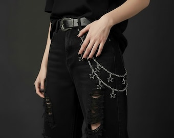May include: Black distressed jeans with a silver chain belt featuring star charms. The belt is paired with a black leather belt with a decorative buckle. The jeans have ripped details.