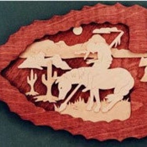 May include: A wooden arrowhead-shaped wall hanging with a layered design. The outer frame is reddish-brown, surrounding a scene of a Native American on horseback, trees, and a cactus, all in lighter wood tones.