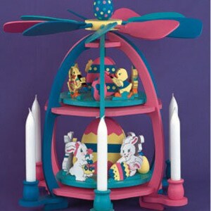 May include: A two-tiered wooden Easter pyramid with a pink and blue egg design. The top tier features two yellow chicks and a red and white striped egg. The bottom tier features two white bunnies and a yellow and white striped egg. The pyramid has six white candles and a blue and pink propeller on top.