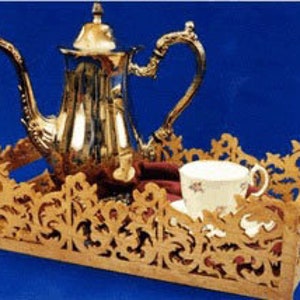 May include: A silver tea pot with ornate detailing sits on a wooden tray with a decorative, openwork design. A white teacup with a floral pattern rests on the tray. The background is a solid blue.