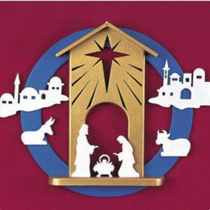 May include: A wooden nativity scene with a gold-colored stable, a blue circular background, and white cut-out figures. The scene includes Mary, Joseph, baby Jesus, and animals. The background is a deep red.