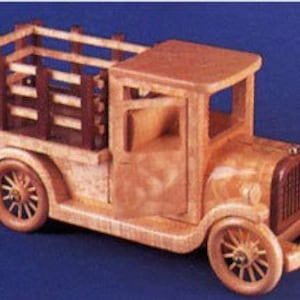 以下が含まれることがあります： 茶色の木製の荷台と茶色の木製の柵が付いた木製の玩具トラック。トラックには、ドアと2つの車輪が付いた薄い茶色の木製のキャビンがあります。トラックは青い背景の上にあります。