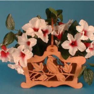 May include: Wooden planter with a carved cardinal design and a handle. The planter is filled with white flowers with red centers.
