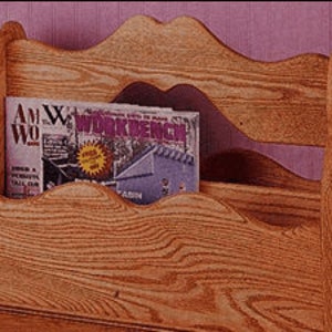 Pode incluir: Revisteiro de madeira com a parte superior e laterais onduladas. O revisteiro é feito de madeira clara e contém uma revista com o título "Workbench". O revisteiro tem uma aparência rústica e artesanal e foi projetado para guardar revistas ou outros materiais de leitura.