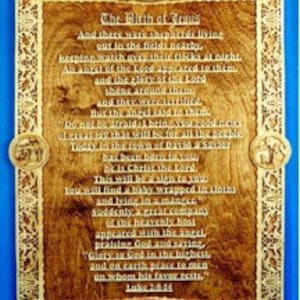 May include: A wooden plaque with a carved design and a blue background. The plaque features a poem about the birth of Jesus, with the text "The Birth of Jesus" at the top and "Luke 2:8-14" at the bottom.