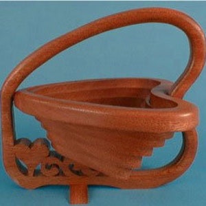 May include: A wooden heart-shaped basket with a handle. The basket is made of multiple layers of wood and has a decorative design on the bottom.