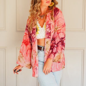 Może przedstawiać: Kobieta w różowym i fioletowym kimonie z kwiatowym wzorem, białym koronkowo-dzianym topem i jasnoniebieskimi dżinsami.