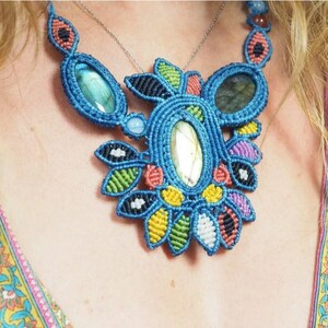 May include: A colorful macrame necklace with a large, iridescent gemstone pendant. The necklace is made with blue, green, yellow, red, and white cord. The pendant is surrounded by smaller, colorful stones.