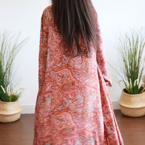 Puede incluir: Una larga bata de manga larga con estampado paisley naranja y rosa.