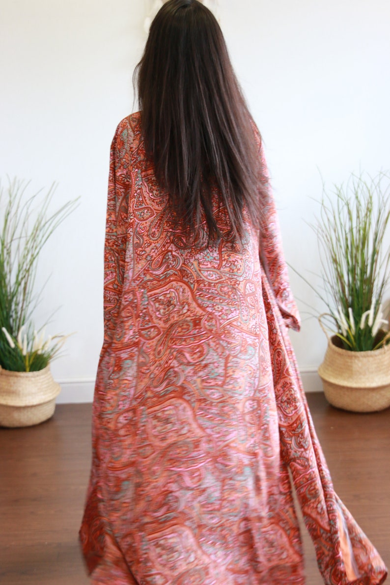Puede incluir: Una larga bata de manga larga con estampado paisley naranja y rosa.