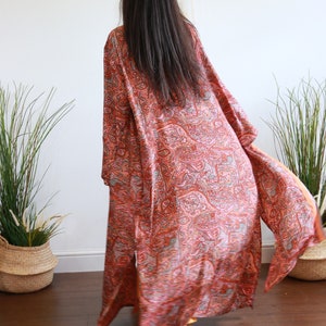 Puede incluir: Un kimono largo y fluido con estampado de paisley en tonos naranja, rosa y gris. El kimono est&aacute; hecho de una tela suave y sedosa y tiene un corte holgado.