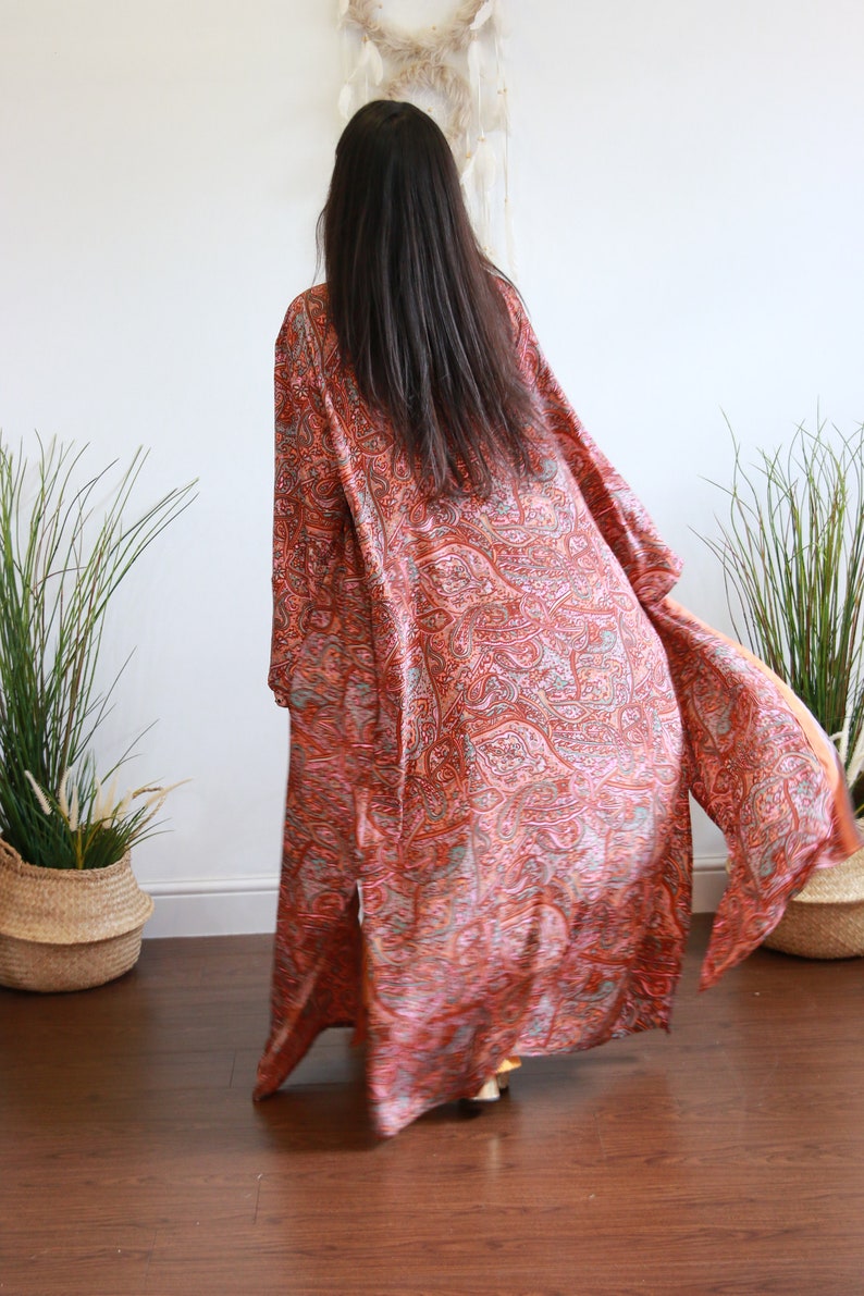 Puede incluir: Un kimono largo y fluido con estampado de paisley en tonos naranja, rosa y gris. El kimono est&aacute; hecho de una tela suave y sedosa y tiene un corte holgado.
