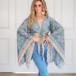 Może przedstawiać: Bluzka w niebiesko-różowy wzór z długimi, szerokimi rękawami i wiązaniem w talii. Bluzka jest noszona z niebieskimi dżinsami.