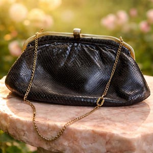 Könnte beinhalten: Schwarze Clutch mit goldfarbenem Verschluss und Kette. Die Tasche hat ein strukturiertes, schlangenlederartiges Muster. Der Hintergrund ist verschwommen, mit Andeutungen von rosa Blumen und Sonnenlicht.