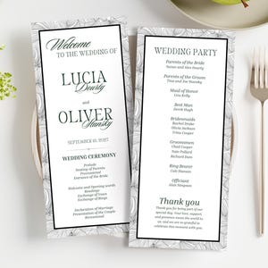 Op de afbeelding: Twee huwelijksceremonieprogramma's met bloemenrandontwerpen. De programma's zijn wit met zwarte tekst, inclusief de namen Lucia en Oliver, en de datum 8 september 2017. Een vork en mes staan rechts.