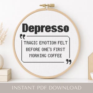 Puede incluir: Un bastidor de bordado circular de madera que contiene tela blanca con texto negro en punto de cruz que dice: Depresso. Tragic emotion felt before one's first morning coffee. El diseño está encerrado en un borde rectangular negro con comillas.