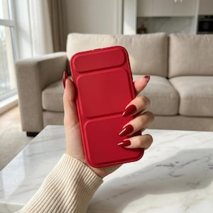 May include: A bright red phone case with a rectangular design. The case has a segmented appearance, with three distinct rectangular sections. The case is held in a hand with red nail polish, suggesting a focus on fashion and accessories.