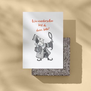 Peut inclure: Une carte de vœux blanche avec une illustration en noir et blanc d'un bouffon tenant un miroir. La carte porte le texte rouge "Wie wunderschön bist du denn, bitte ?" La carte est présentée sur un bloc de pierre grise.