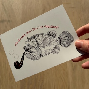 Peut inclure: Illustration en noir et blanc d'un poisson fumant une pipe, avec des motifs complexes. Le texte "Ich denke, also bin ich fabelhaft" est écrit en rouge. L'image est sur une carte blanche.