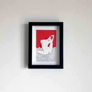 May include: A framed art print featuring a black line drawing of a seated figure against a solid red background. The lower portion of the print displays a detailed pattern of swirling black lines on a white base. The signature A Sim is visible.