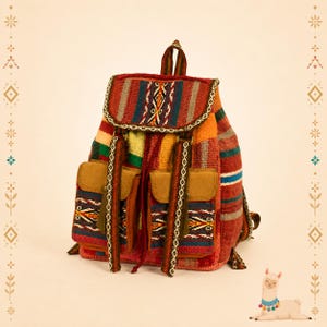 May include: A woven fabric backpack featuring a multi-colored striped pattern in shades of red, orange, yellow, green, and blue. The bag includes a top flap, two front pockets with tan suede-like flaps, and decorative woven straps with geometric designs.