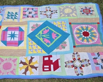Puede incluir: Un edredón de retazos colorido con varios patrones geométricos y florales. El edredón presenta cuadrados con explosiones de estrellas, flores y otros diseños en tonos de rosa, azul, amarillo y verde. Está bordeado con una tela azul claro.