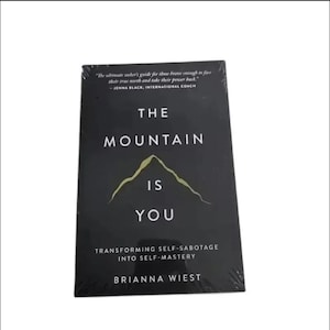 Puede incluir: Un libro negro titulado "The Mountain Is You" con texto blanco y un gráfico de montaña. El subtítulo del libro es "Transformando el autosabotaje en autogobierno" de Brianna Wiest. También se incluye una cita de Jenna Black.